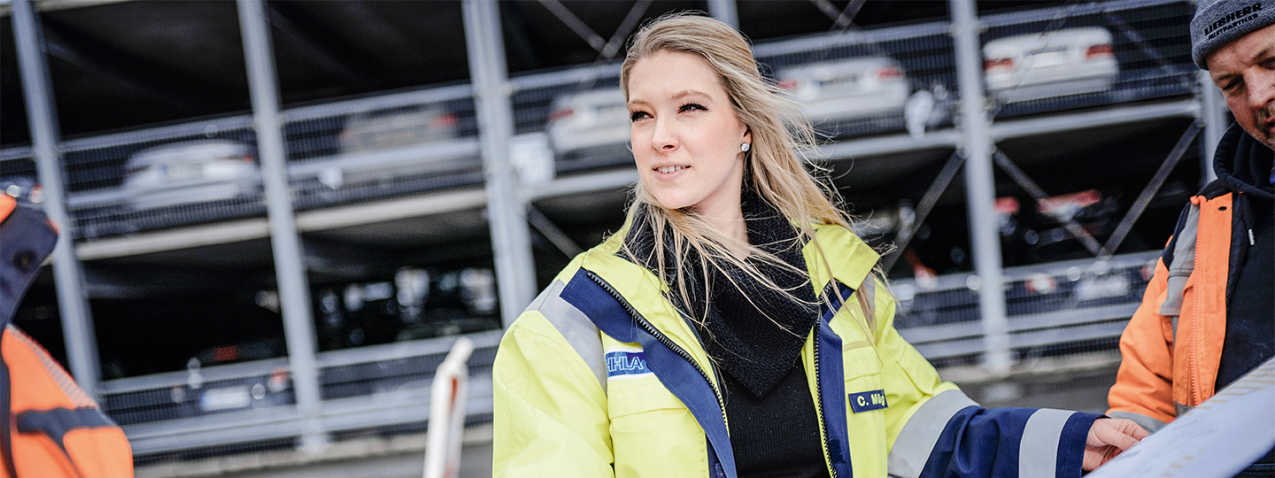 Christina Mügge stands in front of a garage and looks at plans with colleagues. (Photo)