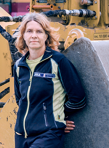 Liivika Mäemurd stands in front of a yellow wheel loader in Estonia. (Photo)
