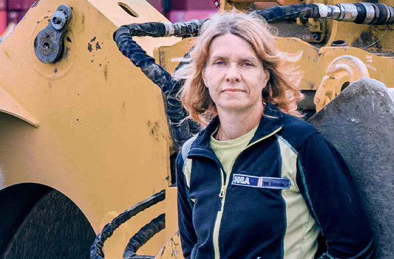 Liivika Mäemurd, crane operator HHLA TK Estonia, stands in front of a yellow wheel loader in Estonia. (Photo)